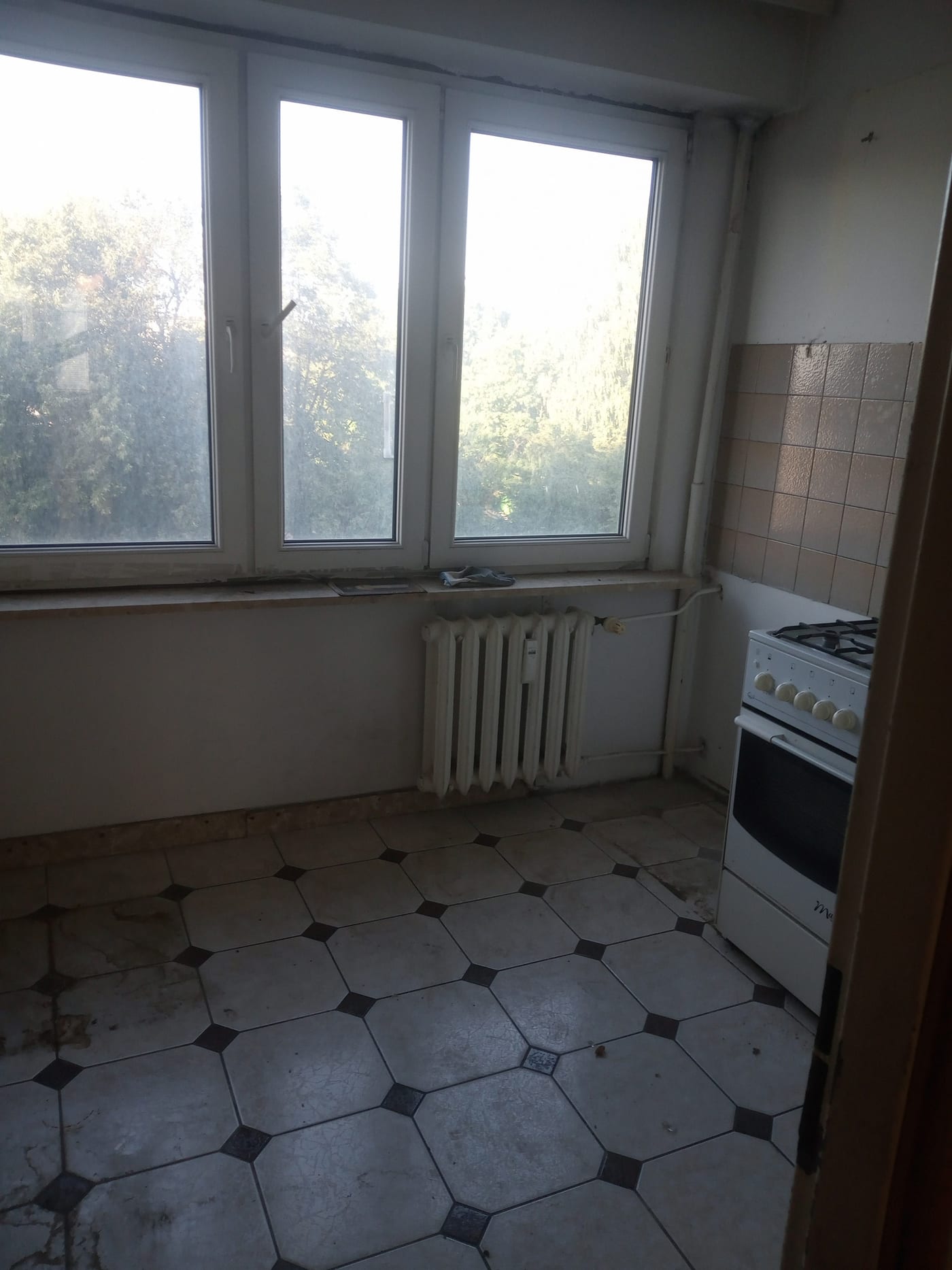 Pusta kuchnia ze starą kuchenką i płytkami na podłodze, po wyniesieniu wyposażenia