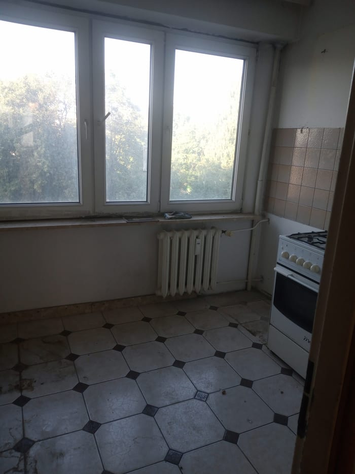 Pusta kuchnia ze starą kuchenką gazową i płytkami na podłodze