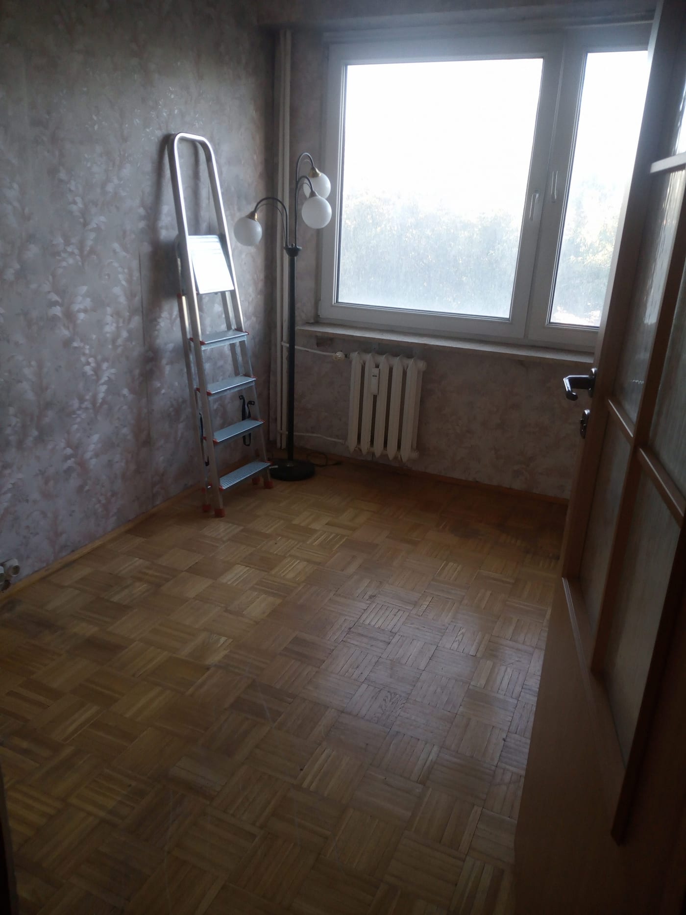 Pusty pokój z parkietem i drabiną pod ścianą, po opróżnieniu