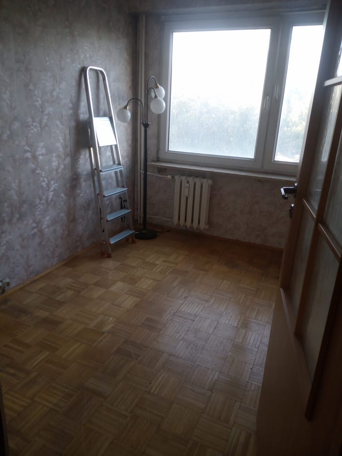 Pusty pokój z parkietem, grzejnikiem pod oknem i drabiną przy ścianie
