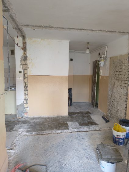 Korytarz ze skutą posadzką, ścianą odsłoniętą do cegły i wiadrami na gruz