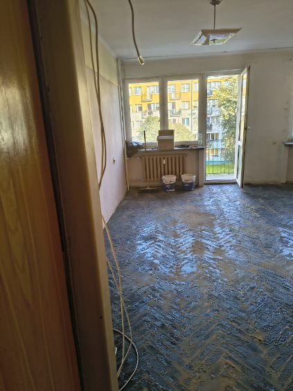 Pusty pokój z drzwiami balkonowymi i śladami kleju w jodełkę na posadzce po zerwanym parkiecie