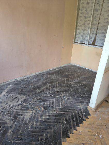 Posadzka ze śladami kleju po parkiecie, w rogu kadru próg i zachowany parkiet w jodełkę