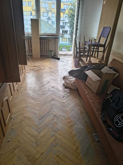 Pokój z parkietem w jodełkę, kartonami, workami i ostatnimi meblami pod ścianą