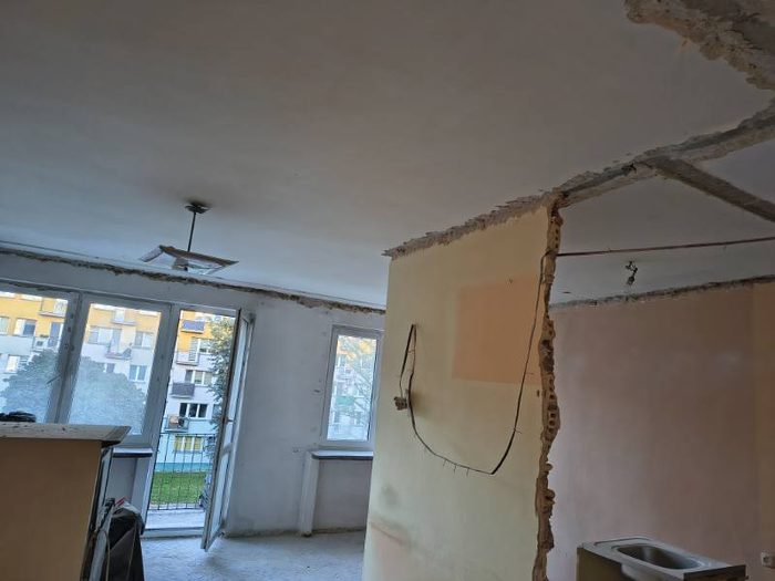 Pokój z oknami balkonowymi, ślady po wyburzonych ściankach na suficie i zlew kuchenny w rogu